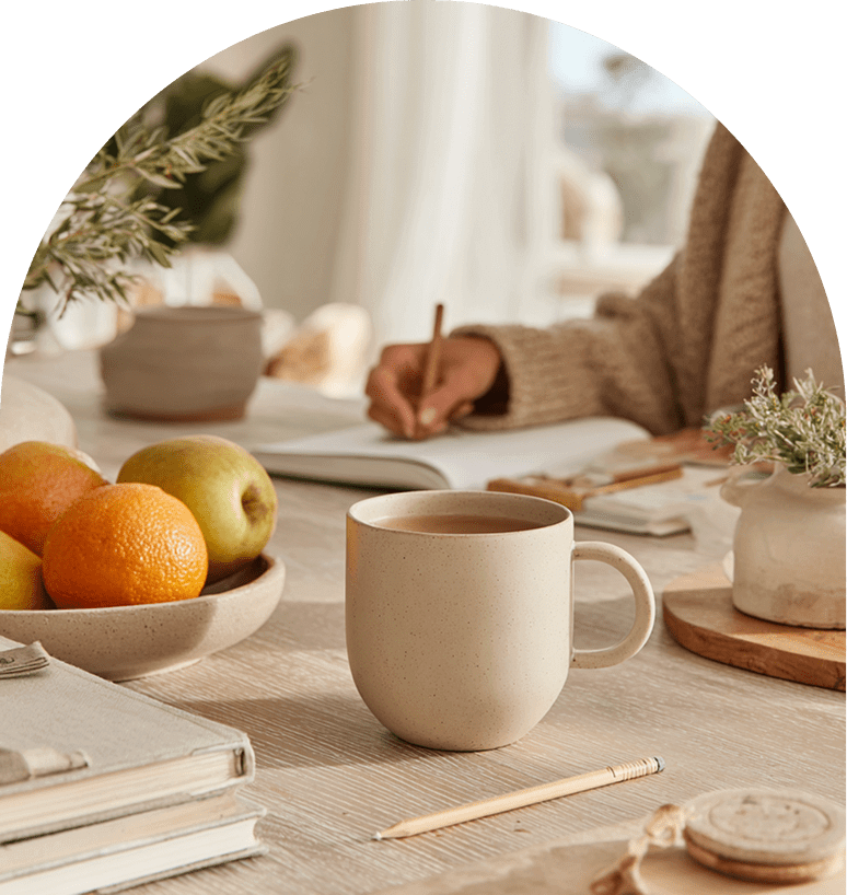 Cozy workspace with coffee, a notebook, and fresh fruit on a wooden table.