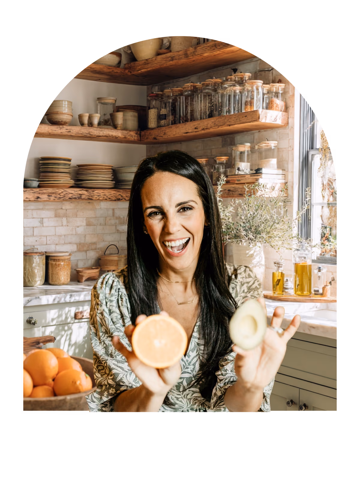 Woman holding citrus and avocado in kitchen.
